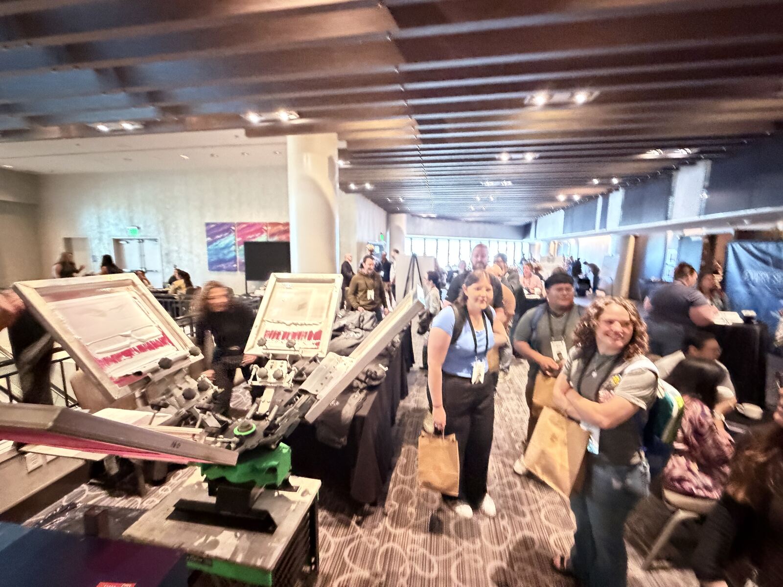Busy event floor showing multiple screen printing and DTF demonstration stations with a crowd observing