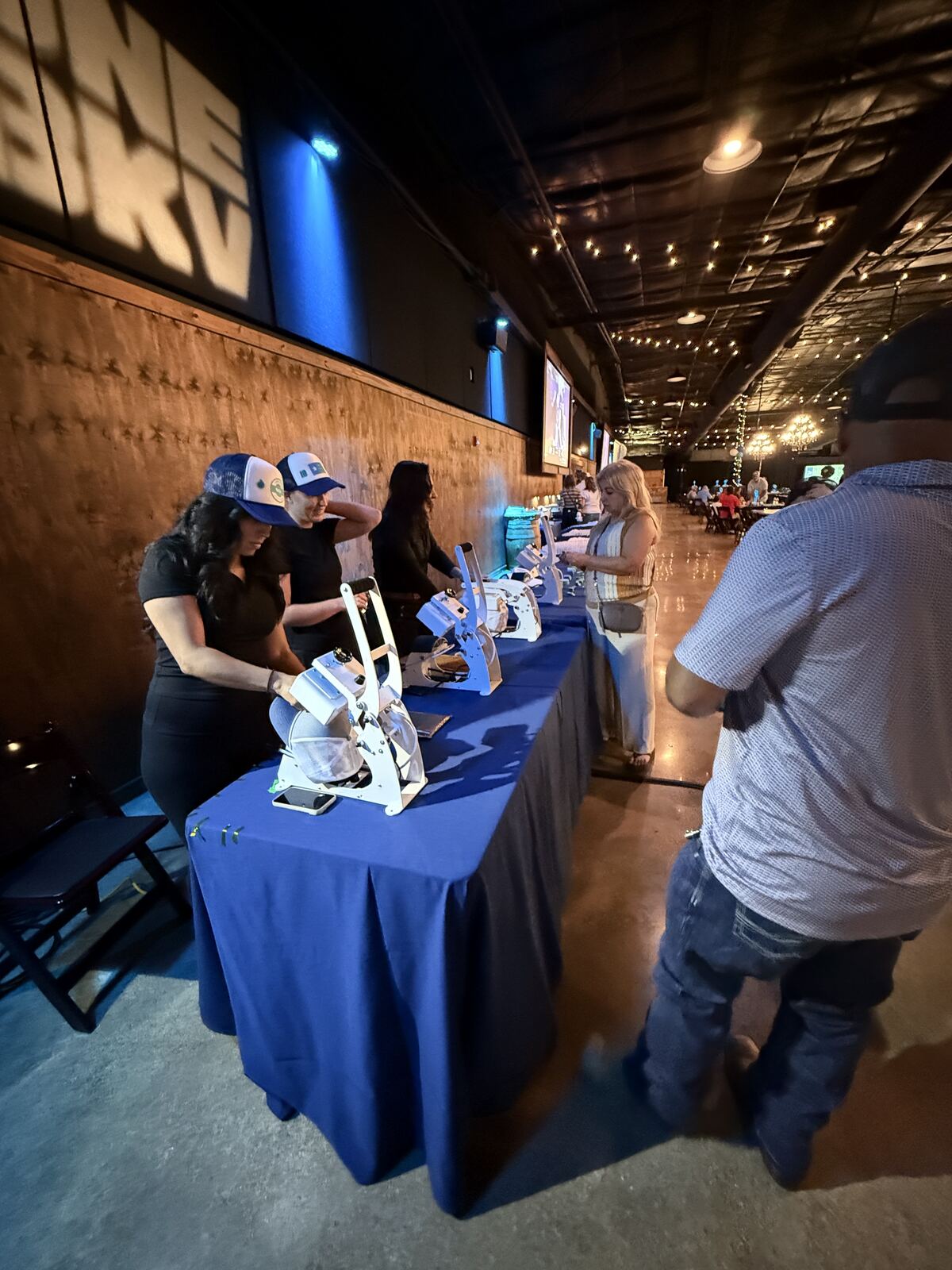 Nighttime event booth with decorated t-shirts displayed on a table with attendees and lighting effects